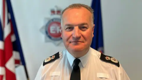 Greater Manchester Police Chief Constable Stephen Watson stands smiling in his uniform. 
