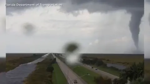 A large tornado hovers in the distance with a motorway in the foreground