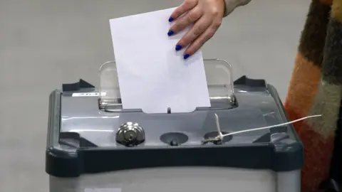 PA Media A woman places a white ballot paper into a vote box