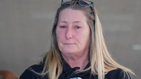PA Media Cheryl Korbel, with long blonde hair and glasses on her head, looks tearfully into the camera