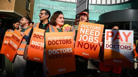 Finnbarr Webster / Getty Images A group of resident doctors strike outside Bristol university hospital on Tuesday morning, they carry placards reading 'doctors need jobs now' and 'pay restoration for doctors'.