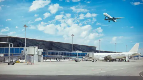 Getty Images A plane in the air and a plane on tarmac at an airport.