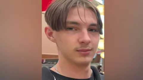 Family handout A young man with short light brown hair with a centre parting. He is wearing a black top and a silver chain. 