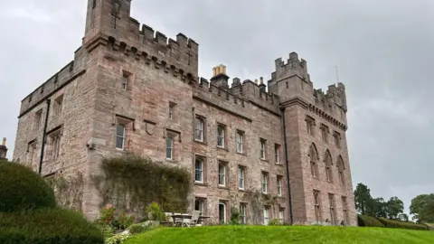 Hutton-in-the-Forest is a grand country home made of stone brickwork, and has parapets. Climbing plants adorn its outer walls.