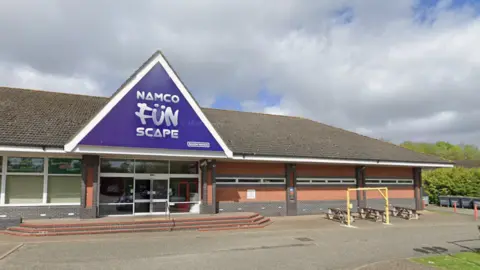 Google A Google Streetview image shows a single-storey brick building with 'Namco Funscape' written in large letters on a triangular ridge above the door. There are also some picnic benches in front and big grey bins around the side.