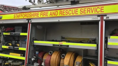 A Staffordshire fire and rescue service engine, with its gear compartments open showing reels and other equipment on show