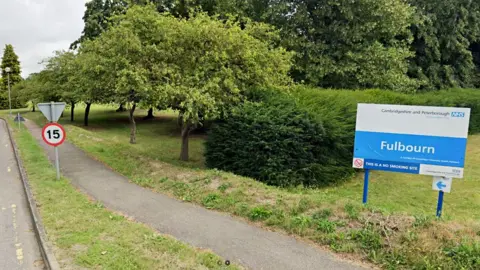 Google A sign at the entrance for Fulbourn Hospital, on the outskirts of Cambridge, on a sliproad next to a 15mph sign. In the background are trees.