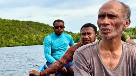 Global Witness Three men, all environmental activists in Indonesia, sit in a small boat and explore the islands in Indonesia's Raja Ampat. Lush forests of the small islands can be seen in the background.