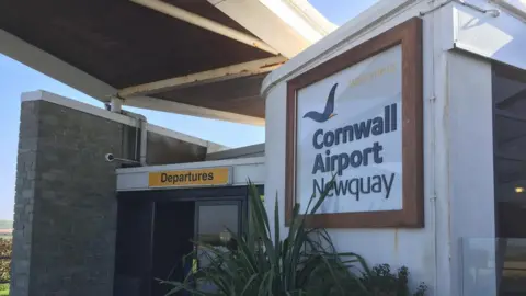 Cornwall Airport Newquay's entrance with sign reading the name of the airport and a yellow rectangle sign reading departures. 