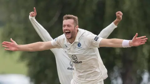Tom Helm stretches out both arms in celebration after taking a wicket for Middlesex