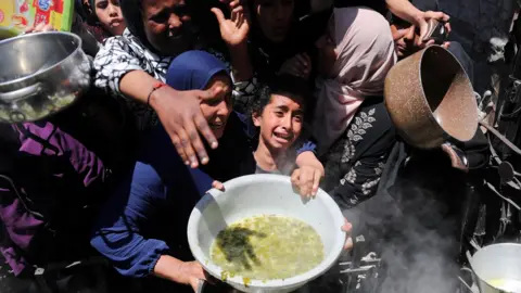 Palestinian receive food cooked by a charity kitchen in Beit Lahia, northern Gaza Strip (8 May 2025)
