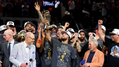 Jalen Brunson #11 of the New York Knicks lifts the Bill Russell NBA Finals Most Valuable Player Award trophy after defeating the San Antonio Spurs in Game Five 