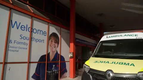 Exterior view of the entrance to Southport and Formby District General Hospital showing an ambulance parked close to the door.