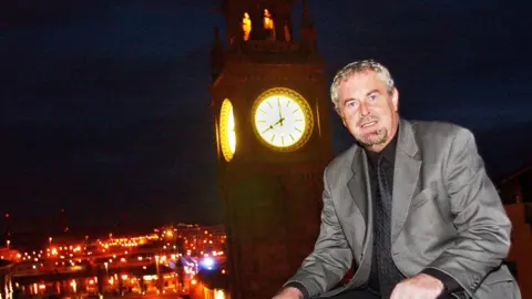 Pacemaker Press A man with short brown and grey hair wearing a grey suit as he sits in front of a lit up clock tower.