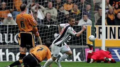 David Rogers/Getty Images Kevin Phillips of West Bromwich Albion celebrates after scoring the opening goal during the Coca Cola Championship play-off semi final first leg match between Wolverhampton Wanderers and West Bromwich Albion at Molineux on May 13, 2007 in Wolverhampton, England. He is wearing a white and navy striped West Brom shirt and players in orange and black Wolves shirts are trying to stop him from scoring. Wolves keeper, wearing red, is on the floor after failing to save the goal. 