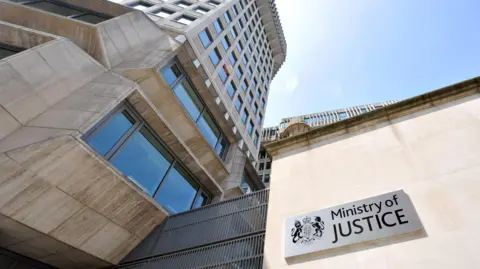 A low-angle image of the Ministry of Justice headquarters in Westminster showing a silver plaque that reads 'Ministry of Justice'
