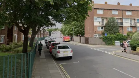 Blocks of flats and terraced houses line Fyning Street and Charles Street which form a T-junction near a small fenced garden.