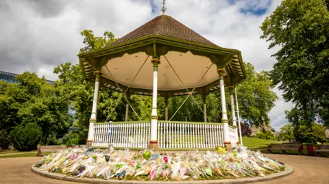 Reading Borough Council Reading Forbury Garden bandstand with hundreds of flowers layed around it.