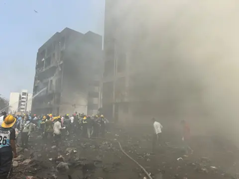 Rescue team members work as smoke rise at the crash site where an Air India plane crashed in Ahmedabad, India