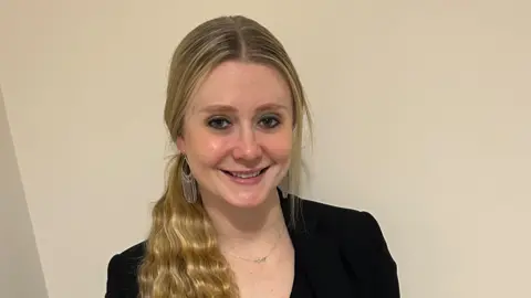 Melanie, a woman with golden shoulder-length hair, wearing a black shirt, smiling for camera.