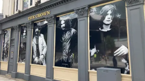 Black and white images of four young men adorn the outside of a pub. All of them have long hair, three have big moustaches.