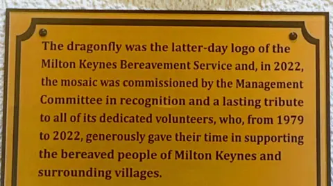 @melaniemosaics A close-up of the golden plaque that hangs underneath the mosaic at the chapel. It has words dedicated to the volunteers who worked for the Milton Keynes Bereavement Service.