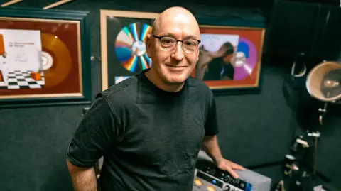 Anthony 'Shorty' Shorter, co-founder & co-owner of Moose Records. He has a shaved head, wears half-rimmed glasses and has a grey, black T-shirt on.