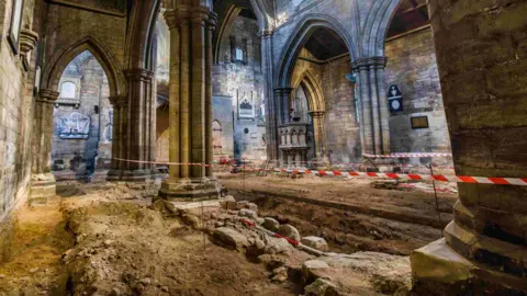 Stuart Boulton Photography The excavations work has exposed walls under the church floor. Red and white tape can be seen stretching between the church pillars to protect the finds.