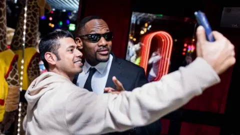 Shad Ellis Shad dressed as Will Smith in Men in Black, posing with a fan for a selfie
