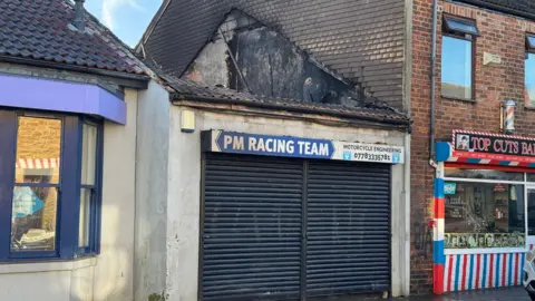 The front of PM Racing Team with the shutter closed. The roof has collapsed.