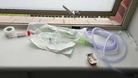 Peter Clarke Tubes and what appears to be a syringe on a hospital window. You can see at least one of the syringes has liquid in.