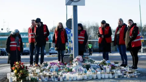 Reuters People stand next to candles and flowers placed near the Risbergska school