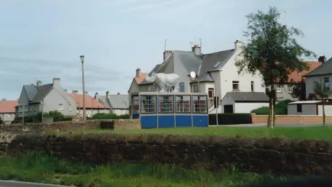 Thomas Nugent A rhino statue on top of a bus shelter in front of a south of Scotland housing scheme