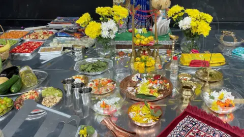 Colourful flowers and food has been laid out as part of an Indian cultural society event, the items are laid out on silver and glass dishes.