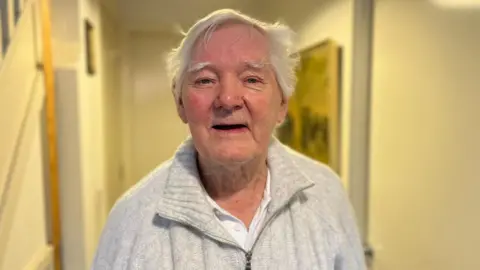 BBC John Morley, who has short grey hair, wearing a grey quarter-zip fleece.