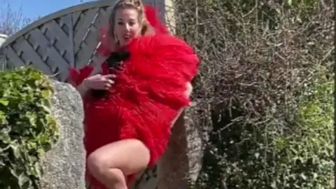 A woman holding a large red boa in a street.