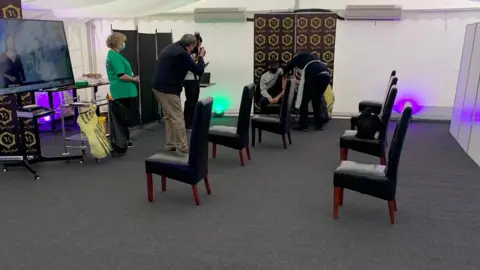 Clifford Rodrigues/V's Punjabi Grill The waiting room for vaccinations with chairs socially distanced and a man receiving his jab in the background