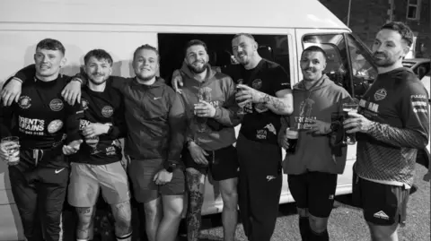 Jekyll Photography A black and white photo of seven friends standing in a row beside a white van, smiling to camera and arms around each other, holding beer glasses