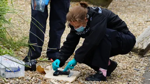 Dan Jessup A police officer with bright blue plastic gloves on inspects a toy gun. 