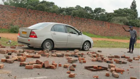 Reuters A police officer stops a car on a rock-strewn road during protests in Harare, Zimbabwe