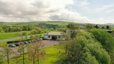 Rowan Glen A factory building with cars parked outside in the Scottish countryside
