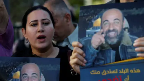People hold up posters of Nizar Banat during a protest in Hebron, in the occupied West Bank, following the activist's death in custody (27 June 2021)