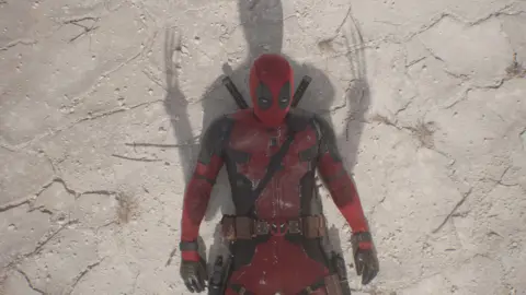 Disney Deadpool lays on the floor with a Wolverine shadow cast over him