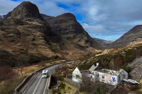 Getty Images The cottage sits above the A82 in a dramatic mountain landscape. The property's white walls are covered in graffiti. 