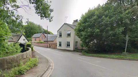 The start of Mill Lane, Mobberley, in Cheshire, showing a property with a thatched roof on the left and on the right some trees then two properties  