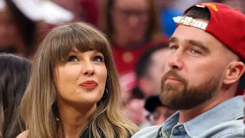 Getty Images Taylor Swift and Travis Kelce posing for camera whilst sat at a basketball game.