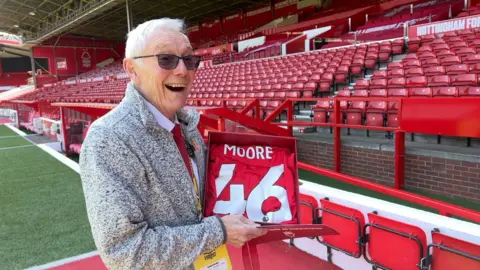 Alan can be seen holding up a shirt with his name and the number 46 printed on the back 