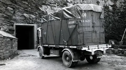 A black and white image of a container truck seen outside a door