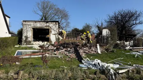 Paul O'Gorman/BBC Firefighters view debris in a rural garden after the blast