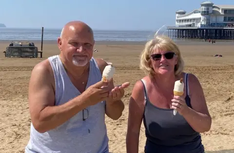 A couple smile at the camera as they hold ice creams on the seafront at Weston super Mare